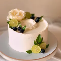 My signature Italian Lemon & Blueberry cake, presented on a stand. This design highlights the freshness of the ingredients with real blueberries, lime slices, and a delicate white flower.