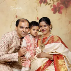 A beautiful traditional family portrait. The mother-to-be is glowing in a white and red saree, surrounded by her husband and son, all in coordinated ethnic wear.