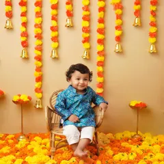A toddler sits happily on a small wicker chair amidst a bed of marigold flowers. His smile and the festive setting make this a perfect milestone photograph.