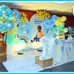 A dreamy hot air balloon-themed first birthday. The stage is set with a large 'ONE' marquee table, a teddy bear in a balloon-basket, and a sky-blue backdrop.
