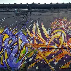 Two distinct graffiti styles side-by-side. On the left, a purple and yellow piece with sharp, aggressive lines, and on the right, an orange and yellow piece with a more rounded, flowing style.