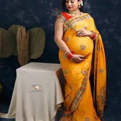 Draped in a vibrant yellow embroidered saree, this mother-to-be radiates joy. The peacock feather she holds is a beautiful symbol of grace and new life, adding a traditional touch to this studio portrait.