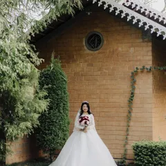 The elegance of a Christian wedding is captured in this full-length portrait of the bride in her beautiful white gown, standing before a rustic brick building.