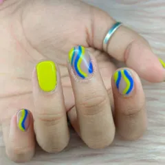 Make some waves with this bright and bold design. This manicure features a solid neon yellow nail and accent nails with a sheer base and artistic waves of blue and yellow.