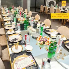 A royal dining setup featuring a long, reflective table adorned with gold-rimmed plates and cutlery. This arrangement is perfect for a formal sit-down dinner, providing a sense of grandeur and exclusivity for your guests.