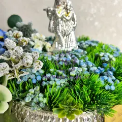 A close-up of our divine Radha Krishna platter, showing the intricate details of the silver idol nestled in a bed of artificial green grass and flowers.