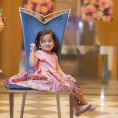 A charming portrait of a little girl in a lovely pink floral dress. I use elegant props like this chair to add a touch of sophistication to children's photoshoots.