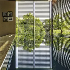 Floor-to-ceiling louvers mediate the relationship between the interior space and the lush landscape outside. They provide a filtered view and protection from direct sun while maintaining a strong sense of connection to nature.