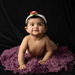 Tummy time during a studio session. This baby looks up with a sweet expression, wearing an adorable strawberry headband that adds a pop of fun to the classic portrait.