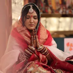 A serene moment captured for a traditional Marwadi bride. The makeup is subtle yet defined, with a focus on flawless skin, a classic red bindi, and defined eyes to complement the royal bridal attire and intricate jewelry.