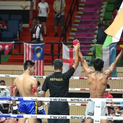 Representing India on the world stage. A powerful moment as our fighter's hand is raised in victory at an international Muay Thai tournament, with the Indian flag held high. We train our athletes to compete at the highest level.