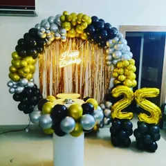 A popular choice for milestone birthdays, this 25th birthday setup includes a full ring backdrop with black, gold, and silver balloons. It's paired with a cake pedestal and foil number balloons on columns.