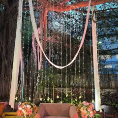 A romantic and dreamy photo booth created by hanging curtains of fairy lights from a large tree. The simple armchair and floral arrangements provide the perfect spot for beautiful portraits.