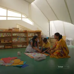A teacher and students engage in a hands-on activity on the floor of a bright, open classroom. The space is designed to be flexible, encouraging different modes of learning and interaction.