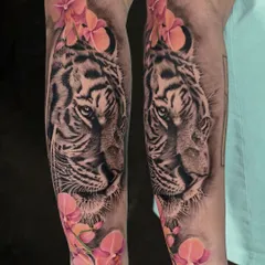 A beautiful blend of styles. This piece features a hyper-realistic black and grey tiger portrait, softened by delicate, color-popped orchid flowers, creating a perfect balance between strength and beauty.