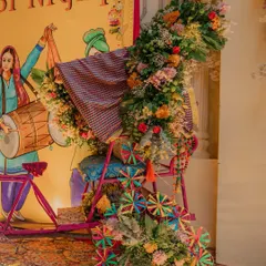 A creative and festive installation for a Punjabi night. A decorated bicycle is adorned with a cascade of flowers and pinwheels, set against a backdrop of vibrant bhangra illustrations.