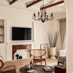 This living room from the Ivy Lane Villa features a custom-built TV unit with a faux fireplace surround. The exposed wooden beams and classic chandelier add to the home's grand, colonial charm.