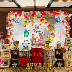 Avyaan's first birthday was a colorful Cocomelon celebration. The setup includes a large backdrop with the whole Cocomelon family, character cutouts, and a vibrant balloon arch with hot air balloon accents.