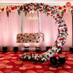 A whimsical floral swing, covered in red, peach, and white roses, suspended from a matching floral arch. A custom neon sign with the baby's name makes it perfect for a naming ceremony.
