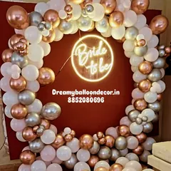 For a modern and trendy look, I use a custom neon 'Bride to be' sign. This is framed by a circular balloon arrangement in rose gold, silver, and white, creating a very chic and stylish party corner.