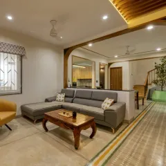 An open-plan living space designed for connection and calm. We crafted the custom grey sectional sofa and the solid wood coffee table to anchor the room, while wooden arches create a seamless flow into the dining area, embodying our warm minimalist approach.