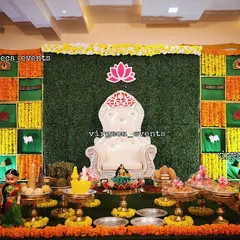 A classic and vibrant setup for a Half Saree ceremony. I use a traditional checkerboard backdrop made with fresh marigold flowers and green fabric, complemented by seer plates, auspicious dolls, and a central lotus motif.
