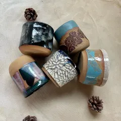 A close-up of five beautifully glazed mugs and cups made by students. The variety of textures and glaze combinations, from floral carvings to abstract drips, is truly inspiring.