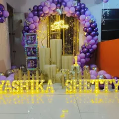 A beautiful and elaborate setup designed for a home celebration. This decor features a full circular balloon arch in purple and gold, a neon sign, and large marquee letters, showing how I can create a grand look in an intimate space.