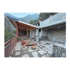 The homestay nearing completion, showing the relationship between the covered wooden veranda and the open stone-paved terrace. The structure is built to follow the contours of the hillside.