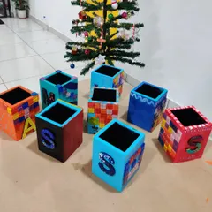 A collection of colorful, personalized pen stands made by kids at a birthday party, displayed in front of a Christmas tree.