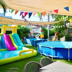 A wide view of our pool party setup, featuring multiple pools and a large inflatable slide under a shaded canopy for comfortable fun.
