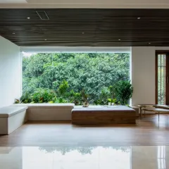 Light seeps in, greens breathe out. This minimalist lounge nook features a large picture window that frames a lush forest view, creating a tranquil space that feels both indoors and out.
