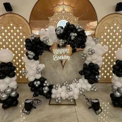 A modern and chic heart-shaped balloon backdrop in a black, white, and silver color scheme. The 'Happy Birthday' neon sign in the center adds a stylish glow, making it a great focal point for a party in a hotel or banquet hall.