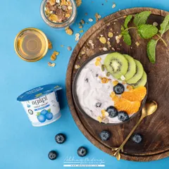 This vibrant yogurt bowl uses a bright blue background to make the colors of the fresh fruit toppings pop. The composition is energetic and full of life.