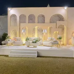 A chic and contemporary stage design for an outdoor event. This custom-built backdrop features layered panels with modern arched cutouts and integrated lighting, furnished with stylish, minimalist seating.