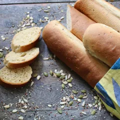 Slices of our in-house whole-wheat baguette, surrounded by the mixed seeds we use. It's simple, rustic, and delicious, perfect for our avocado toast or to enjoy on its own.