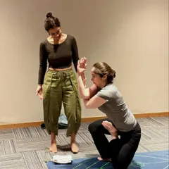 A different angle of the Vatayanasana assist, showing the connection and focus between teacher and student. This is a moment of shared effort and trust.