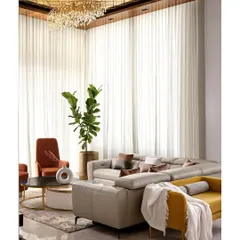 A full view of the 14-foot living room, showcasing the double-height sheer curtains that flood the space with natural light. The layout is designed for comfort and conversation, with a mix of bespoke sofas and accent chairs in contrasting colors.