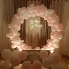 An elegant and minimalist birthday backdrop. This circular arch made of soft pink and white balloons, paired with a "Happy Birthday" neon sign, is perfect for a sophisticated at-home celebration.