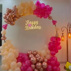 A circular balloon arch is a popular choice for creating a beautiful focal point. Here, a mix of rose gold, pink, and peach balloons with a "Happy Birthday" neon sign creates an elegant and picture perfect spot for any birthday celebration.