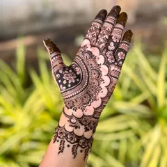 A single hand showcasing a modern henna design. The pattern features a large floral element with a scalloped border, combining fine lines with bold, filled sections for a striking look.