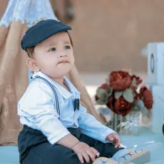 A dapper little boy dressed in a newsboy cap and suspenders enjoys a picnic setup on the sand. We can bring our creative props to any location.