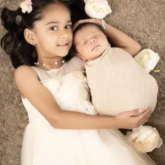 A beautiful overhead shot of a big sister holding her new baby sibling. We use soft, neutral tones to create a dreamy and angelic feel for our newborn and sibling sessions.