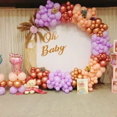 A lovely 'Oh Baby' shower setup for a baby girl. This features a circular balloon arch in pastel pink, purple, and rose gold, with a custom backdrop.