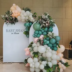 A chic "Baby Shah in Bloom" decoration with a unique color palette. The mix of sage green, peach, and white balloons, combined with fresh flowers and leaves, offers a fresh and modern aesthetic.