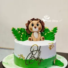 An adorable 'Oh Baby' shower cake with a jungle theme. This cake is topped with a cute fondant lion and decorated with green leaves and gold flakes.