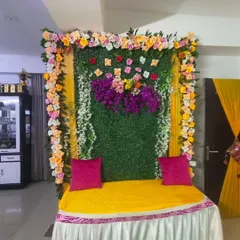 For intimate home functions, I create compact and beautiful backdrops. This one uses a green foliage panel, a frame of colorful flowers, and a comfortable gadda with bright pink cushions for the seating.