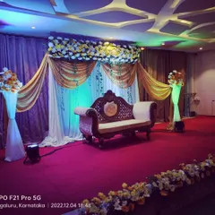 This is a popular stage design for indoor events at convention halls. The combination of golden and white drapes, a floral border, and an ornate carved sofa creates a timeless and regal look.