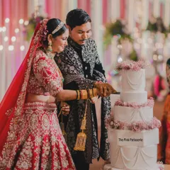 A beautiful moment captured as the happy couple cuts into their five-tiered classic white wedding cake. The cake is elegantly decorated with swags of delicate pink flowers, making it a timeless choice for a grand wedding.