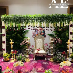 A complete Seemantham (baby shower) setup. This traditional arrangement features a backdrop of fresh banana leaves and jasmine strings, a decorated chair for the mother-to-be, and brass lamps, all surrounded by floral offerings.